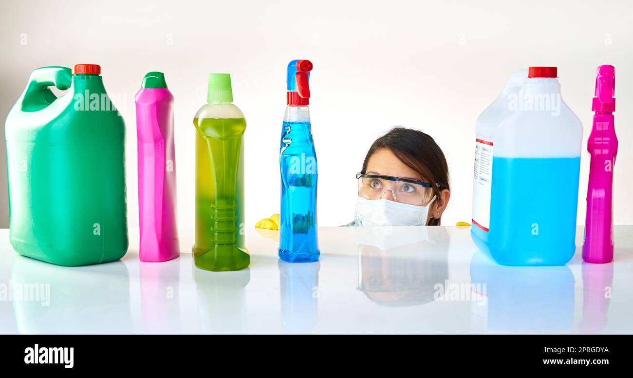 Ha in vista una scelta difficile: Una giovane donna che guarda da dietro un bancone a varie bottiglie di detersivo. Foto Stock