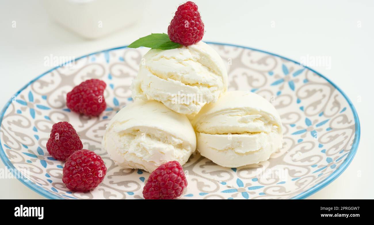 Palline di gelato alla vaniglia con lamponi rossi in un piatto rotondo Foto Stock