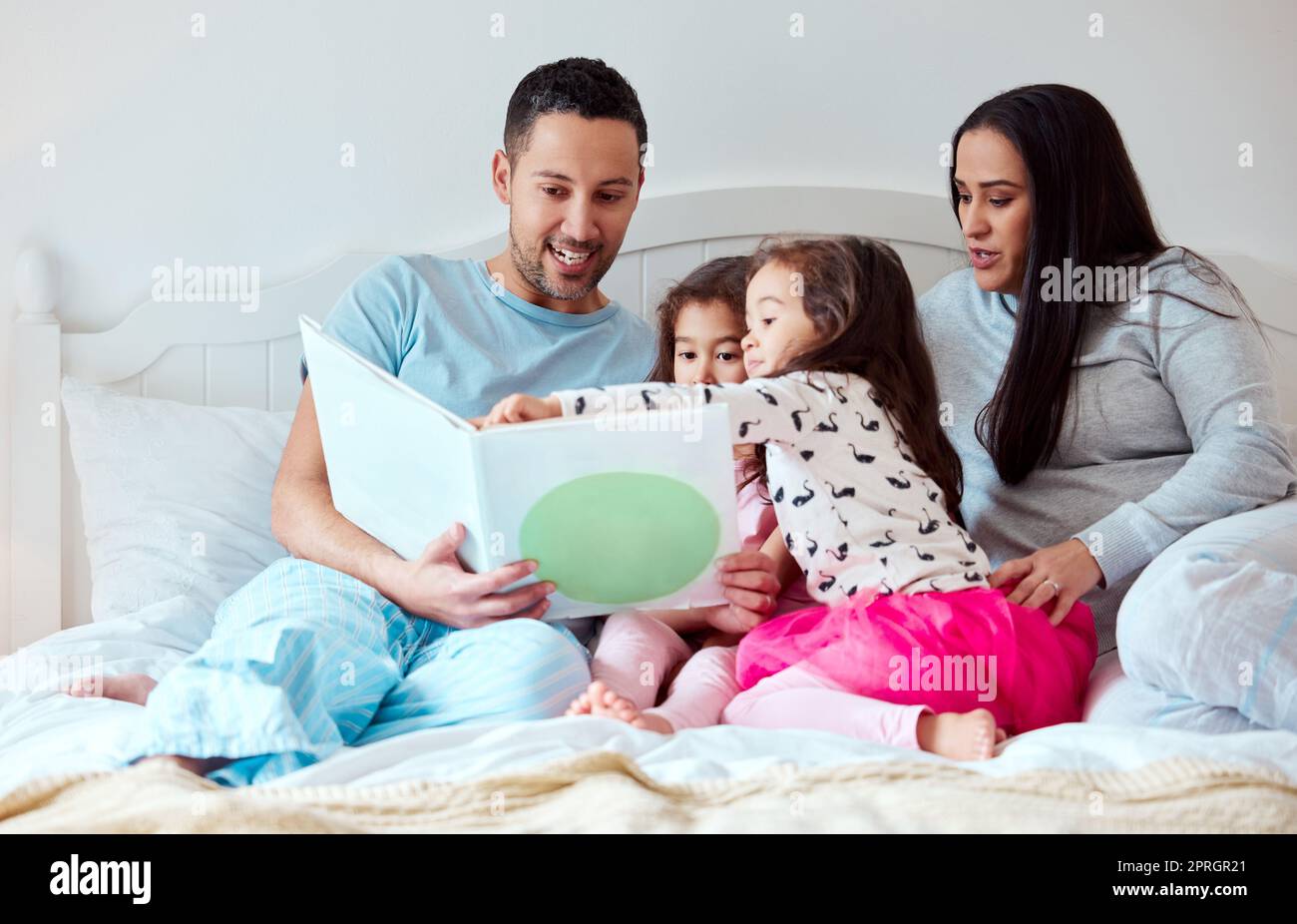 Voglio sapere cosa succederà dopo. un uomo che tiene un libro di storia mentre siede con la sua moglie e due figlie Foto Stock