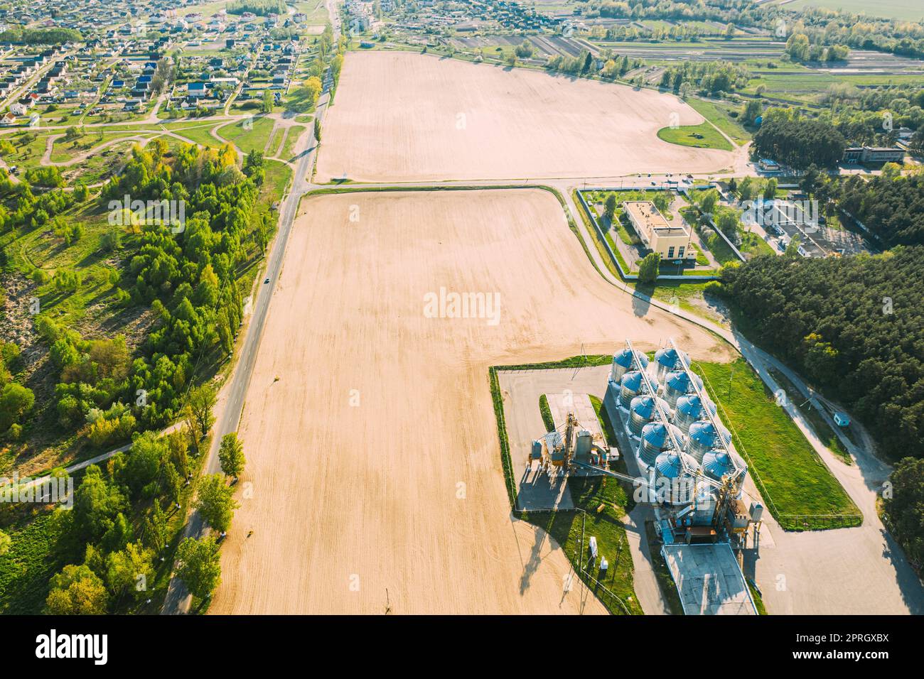 Vista aerea Granaio moderno, complesso di essiccazione dei cereali, cereali commerciali o silos di semi nel paesaggio rurale di Sunny Spring. Essiccatore per mais Silos, Inland Grain Terminal, elevatori per cereali in piedi in Un campo Foto Stock