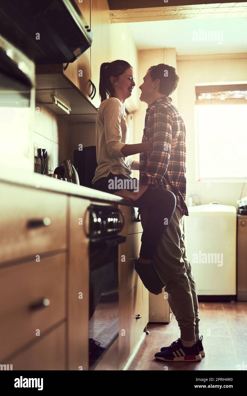 Meno parlare, più baciare, una giovane coppia affettuosa che condivide un momento romantico in cucina. Foto Stock