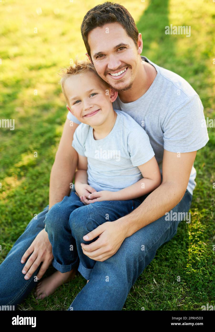 Tempo di qualità con papà. Ritratto di un padre sorridente e di suo figlio seduto sull'erba in un parco. Foto Stock