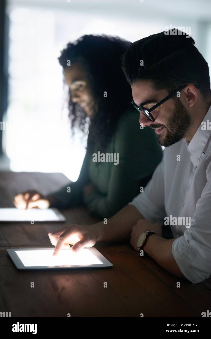 La tecnologia ha portato a una grande quantità di cambiamenti nel business. Due colleghi lavorano tardi sui tablet digitali in ufficio. Foto Stock