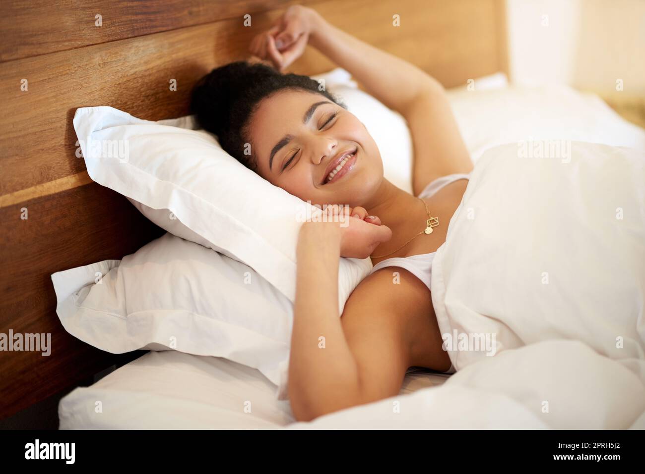 Svegliarsi con la felicità nel suo cuore, una giovane donna felice che si sveglia a letto sentendosi ben riposata. Foto Stock