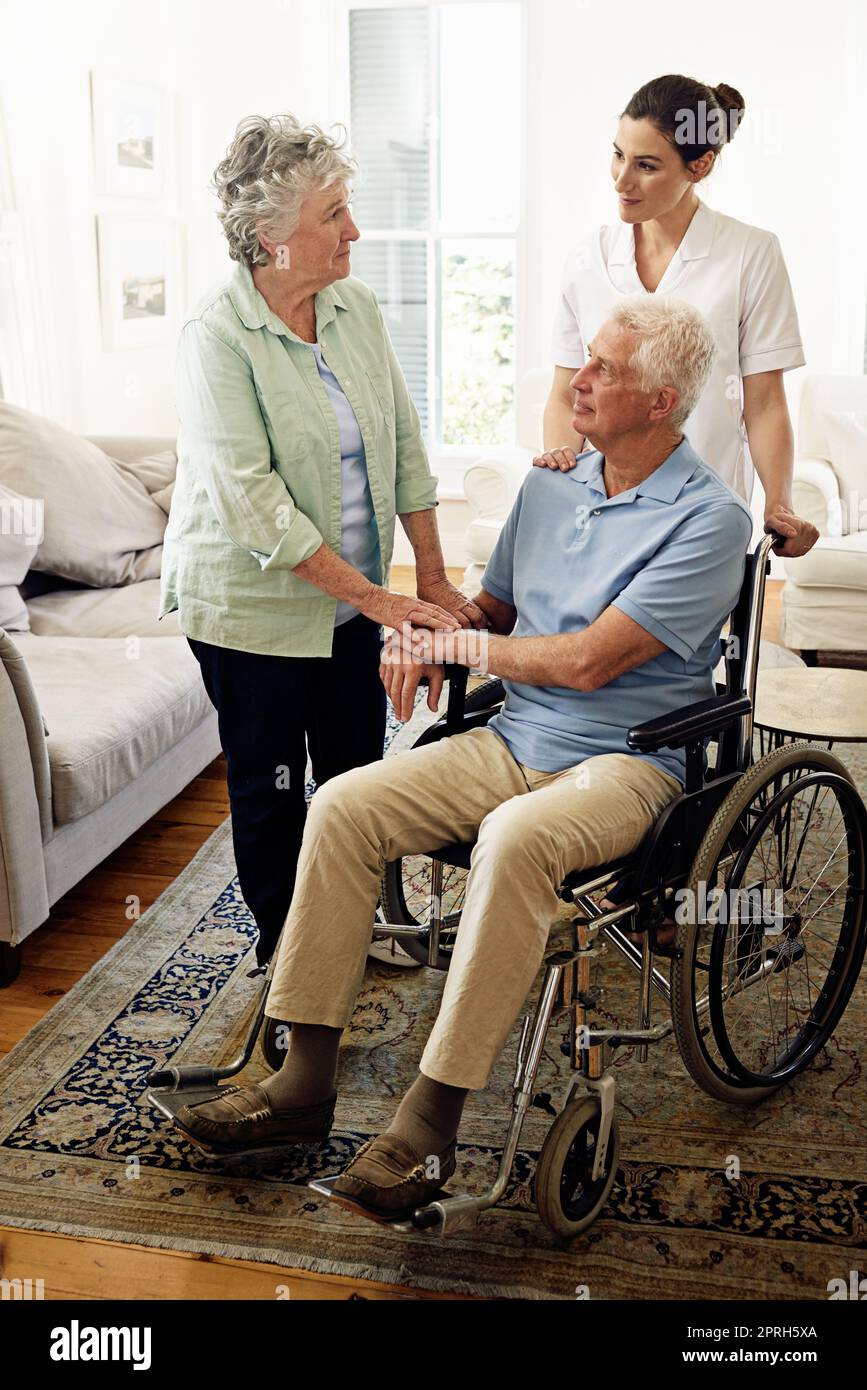 Aiutare gli anziani a vivere una vita piena. Un caregiver sorridente con un uomo anziano in sedia a rotelle e sua moglie a casa. Foto Stock