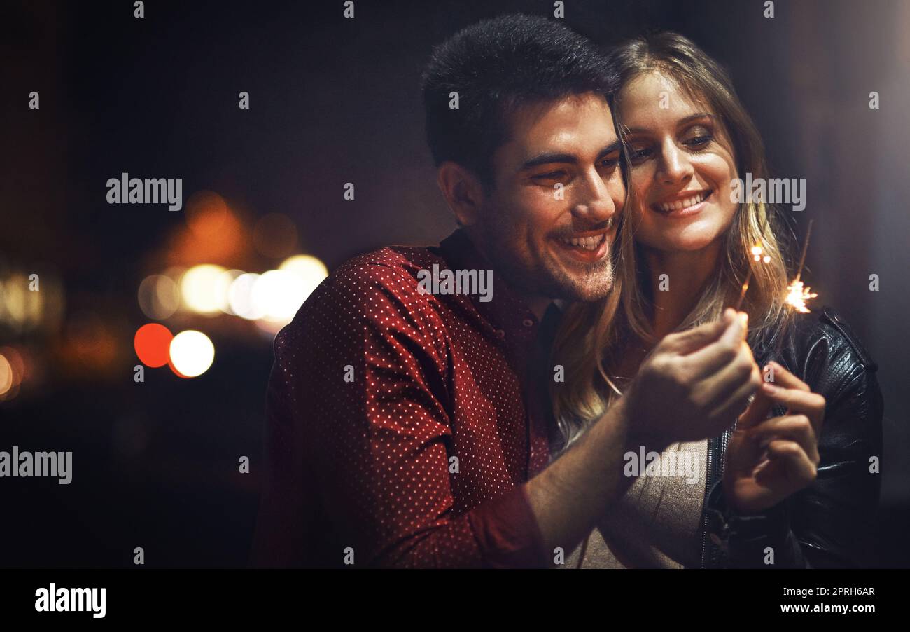 Per celebrare il nostro amore... una giovane coppia felice che festeggia con gli scintillatori fuori di notte. Foto Stock