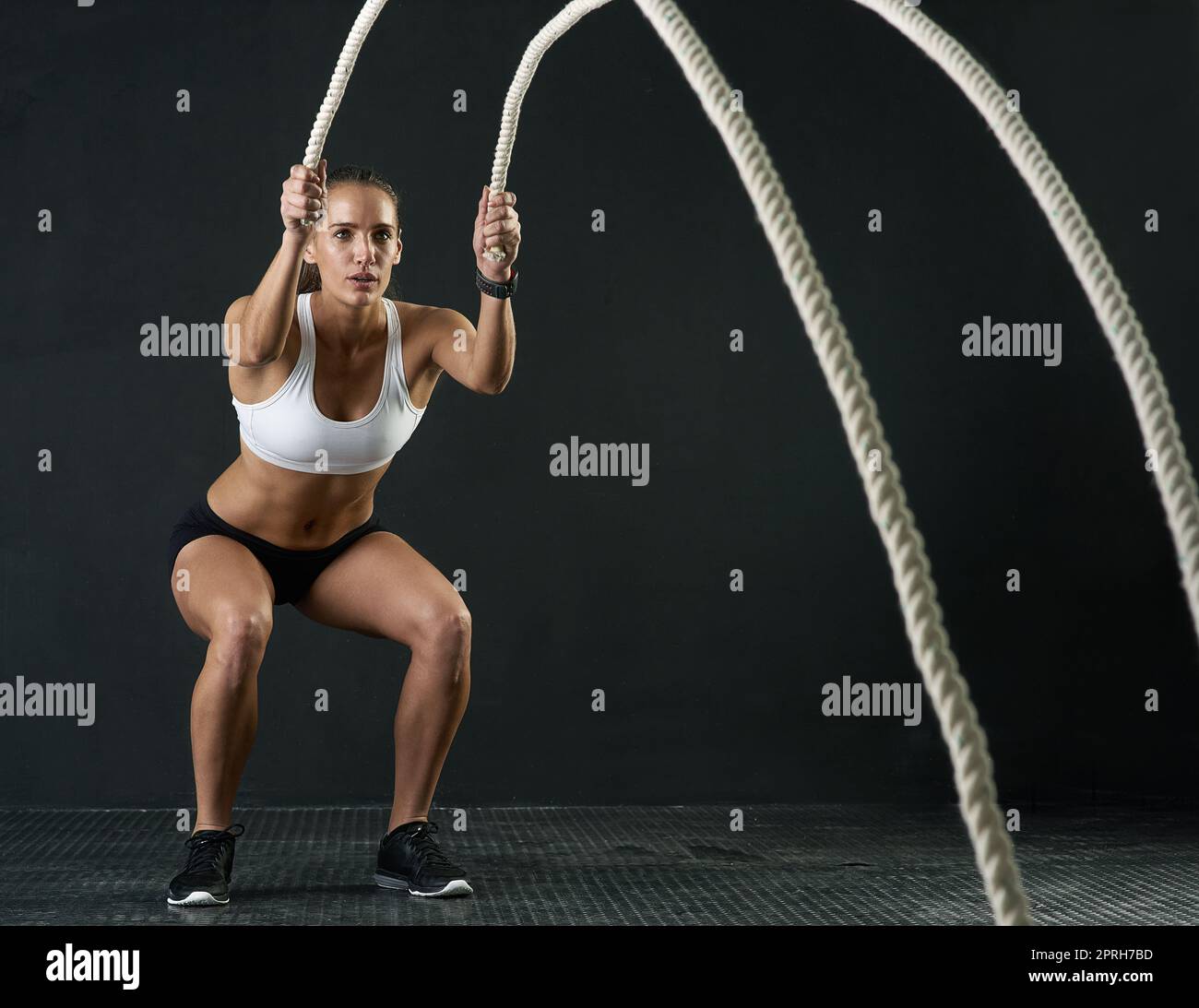 Mettiti in forma. Studio shot di una giovane donna attraente che lavora con corde pesanti su uno sfondo scuro. Foto Stock