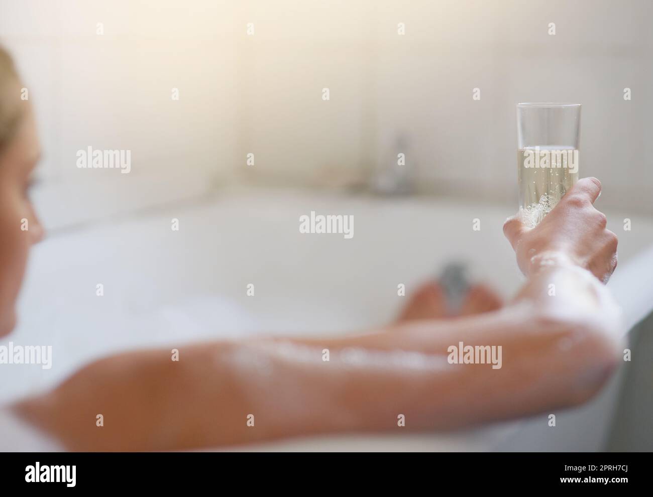 Una giovane donna che si rilassa nella vasca da bagno con un bicchiere di vino. Foto Stock