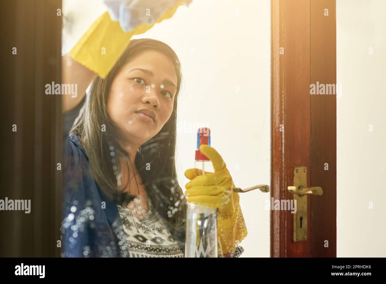 Mantenere le cose spick e span. Una donna che pulisce una porta di vetro a casa. Foto Stock