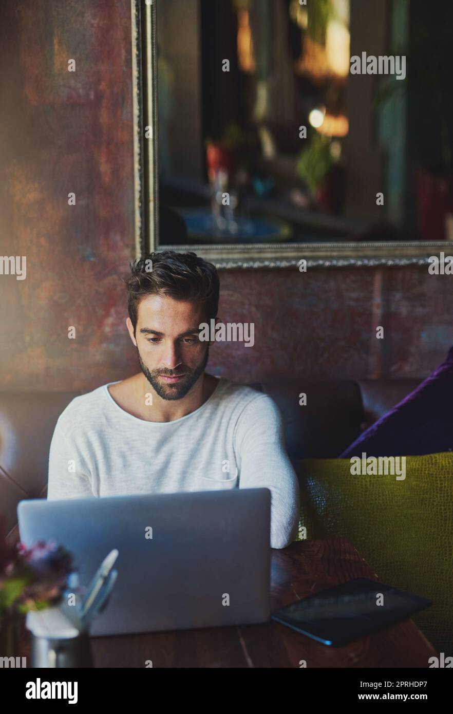 Blogging nel suo tempo libero. Un giovane uomo che usa il suo laptop in un bar. Foto Stock