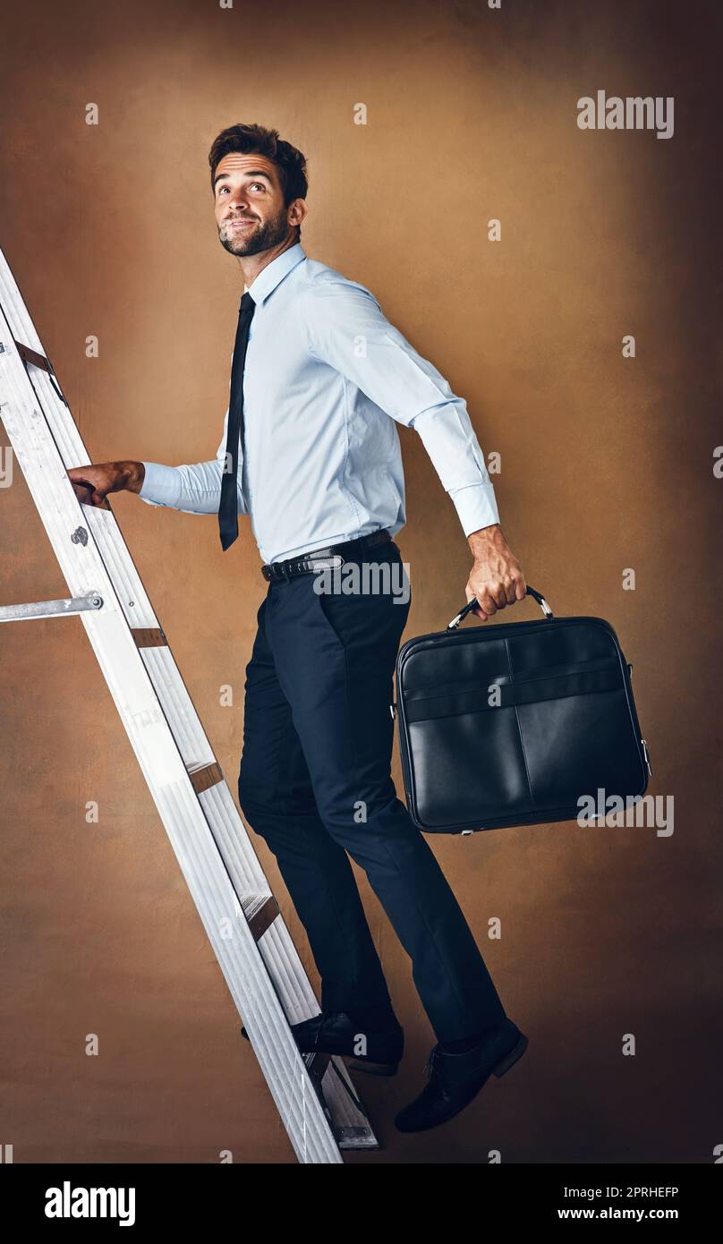 Meglio fare spazio per lui al top. Studio shot di un bel giovane uomo d'affari che sale su una scala su uno sfondo marrone. Foto Stock