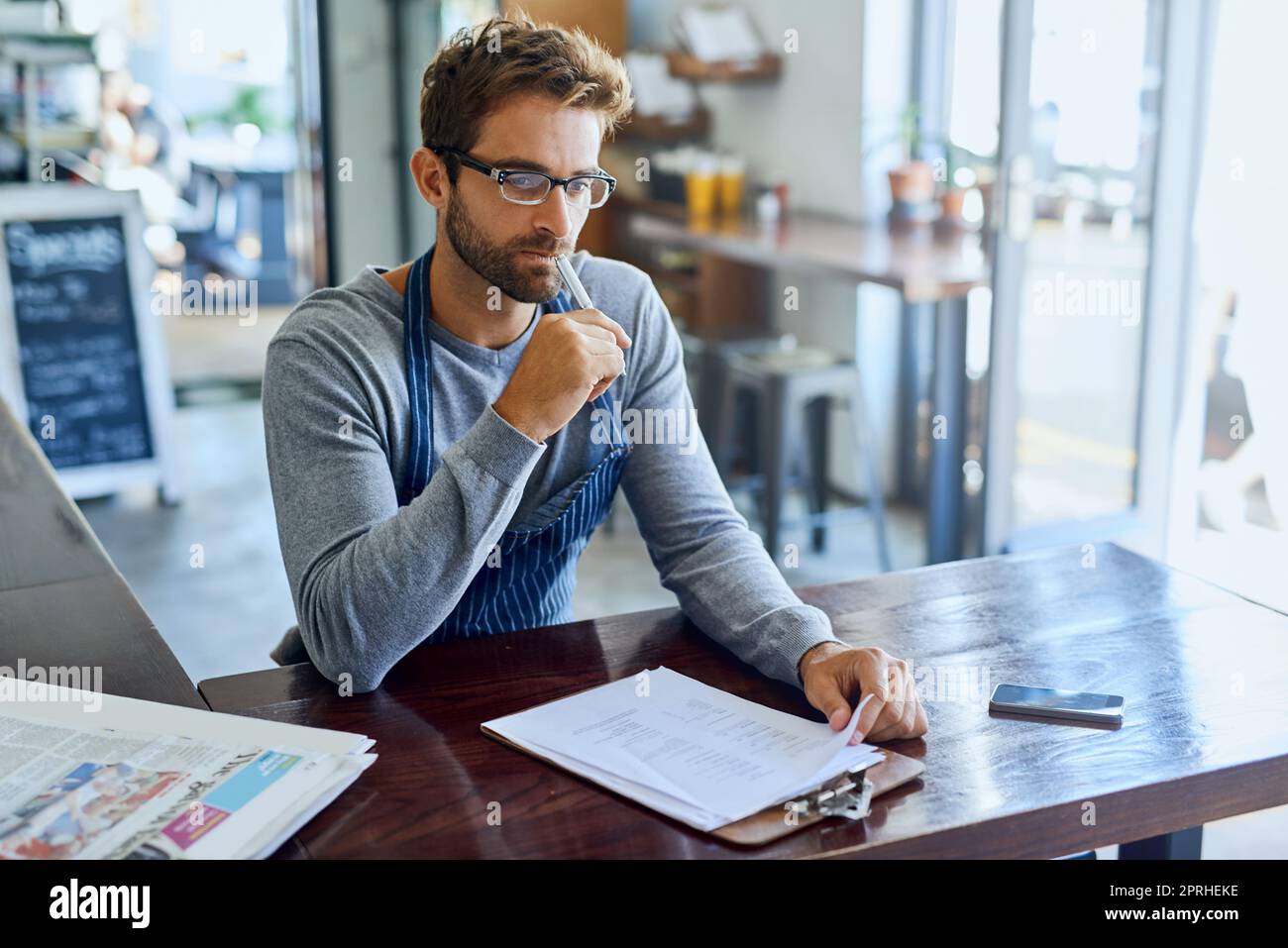 Forse è il momento di espandersi... un bel giovane proprietario di una caffetteria che passa sopra la documentazione. Foto Stock