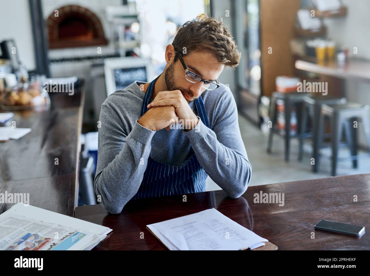Check-in con le cifre mensili. Un bel giovane proprietario di una caffetteria che va oltre la documentazione. Foto Stock