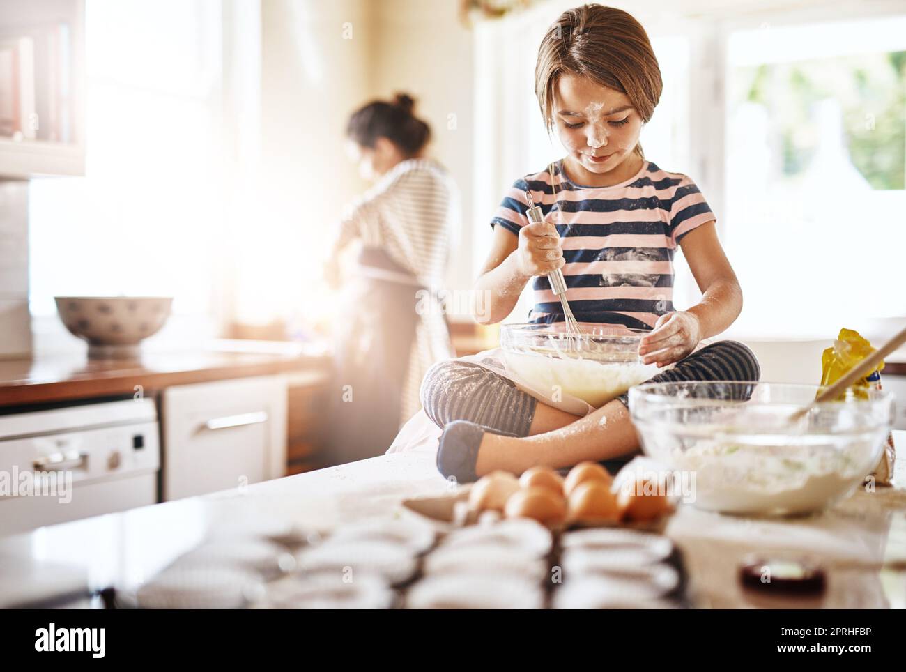 Shes Moms speciale fornaio piccolo. Una bambina che si diverte mentre cuoce con la madre in cucina. Foto Stock