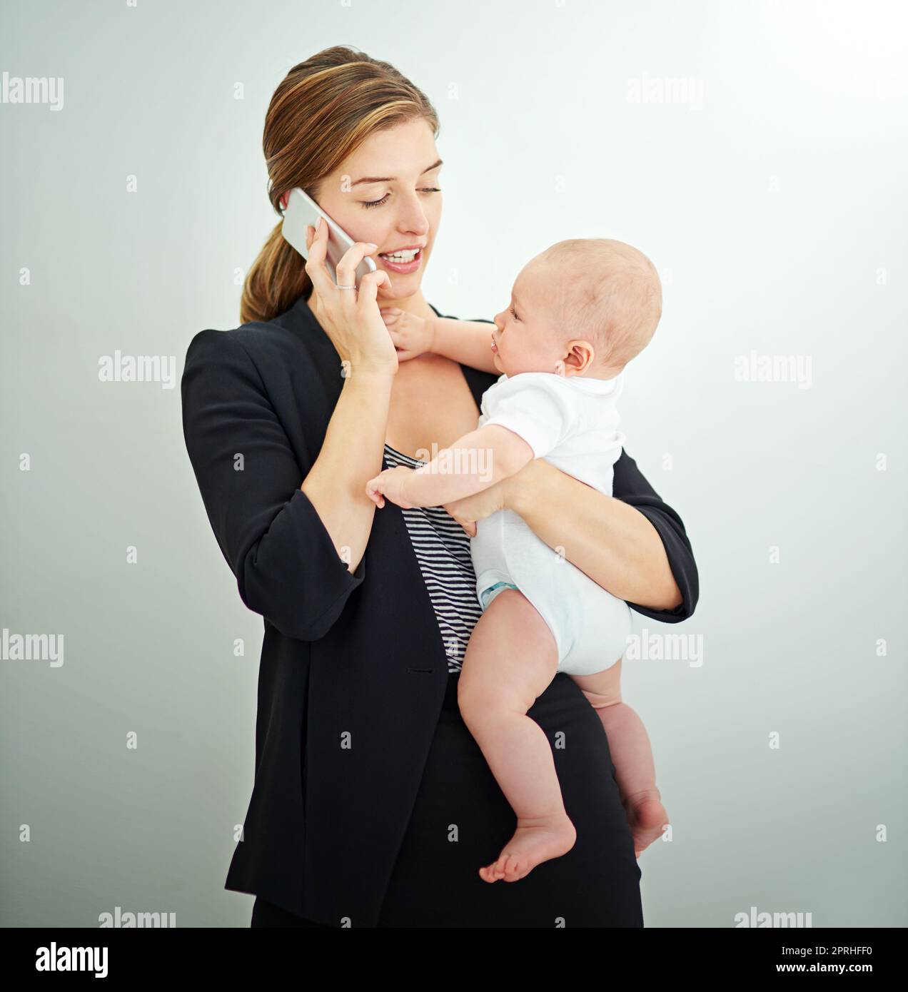 Prendendosi cura del bambino e del commercio. Una giovane donna d'affari riuscita che trasporta il suo bambino adorable mentre parla al telefono. Foto Stock