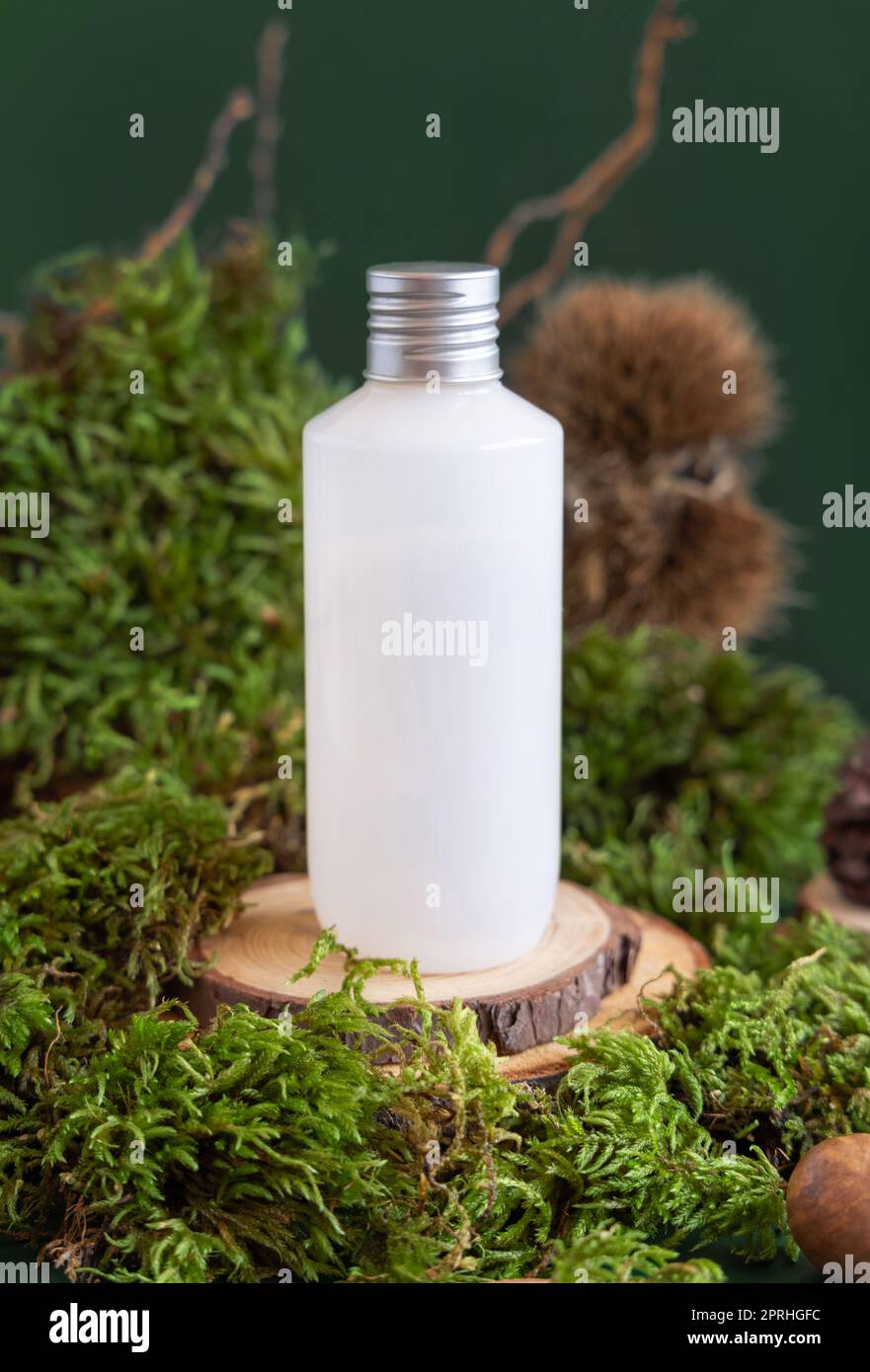 Bottiglia di crema di plastica bianca su un pezzo di legno tra muschio verde, primo piano, mockup cosmetico naturale Foto Stock