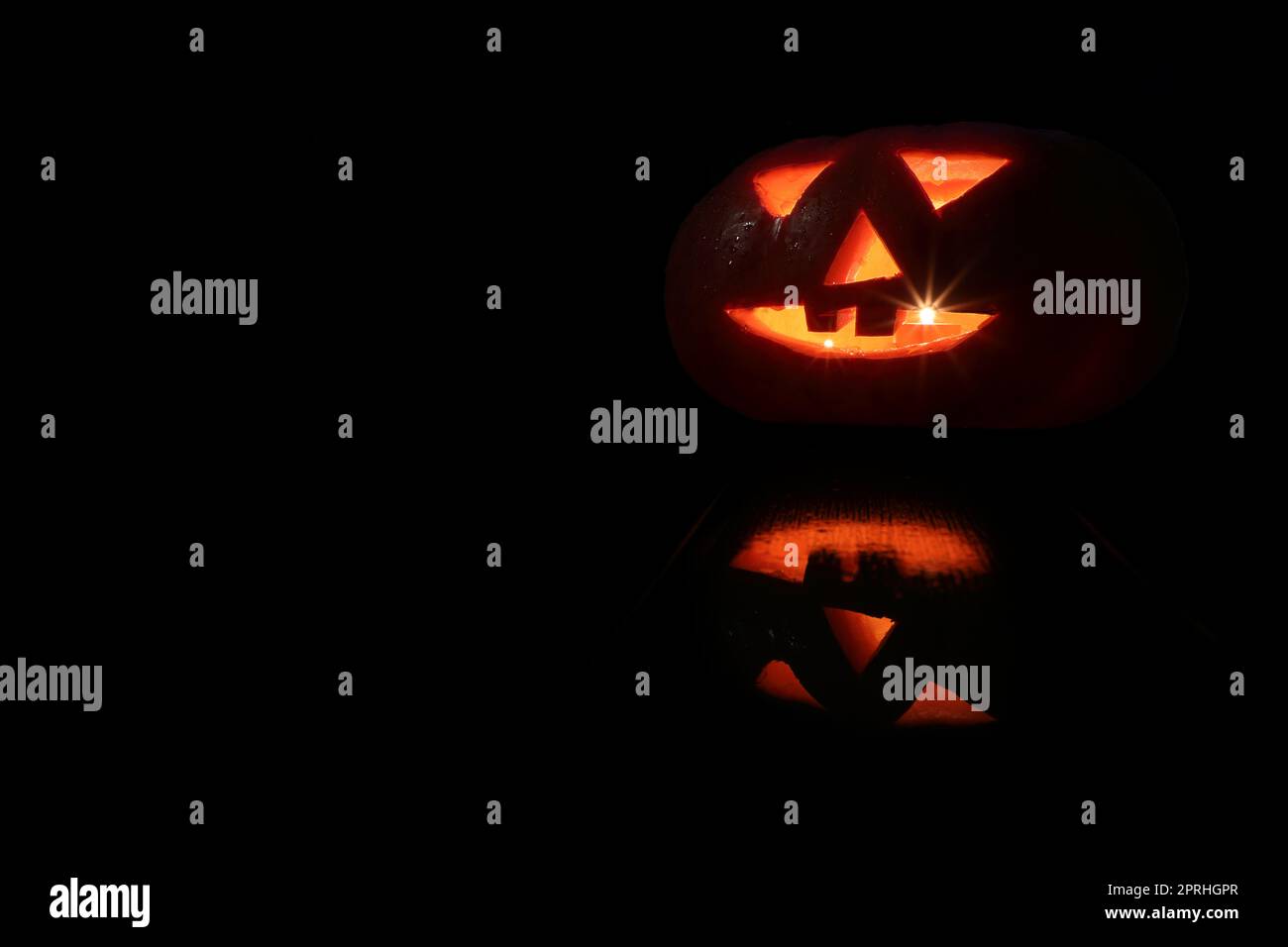 Zucca di Halloween con occhi che illuminano all'interno con riflessi su sfondo nero Foto Stock