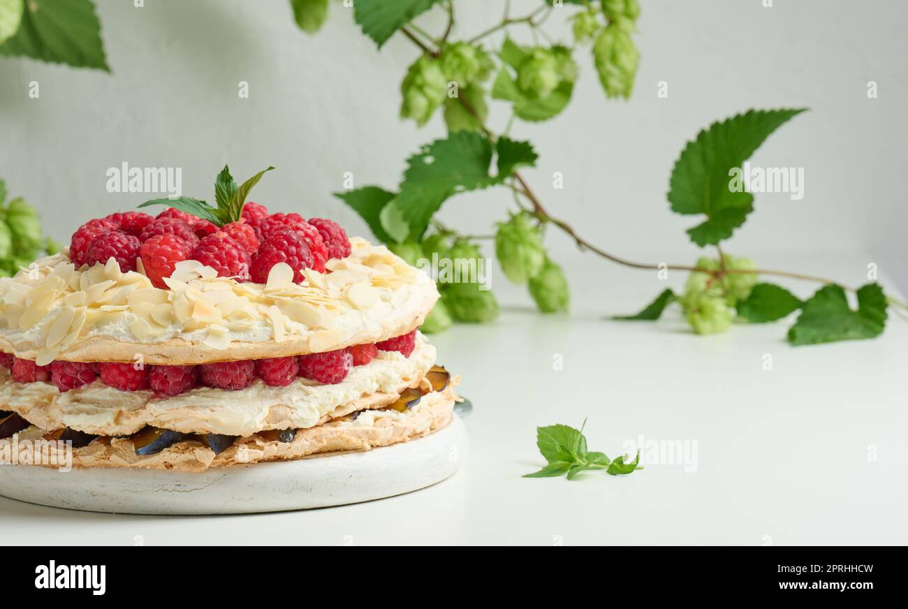 Torta di meringa rotonda con lamponi freschi su sfondo bianco Foto Stock