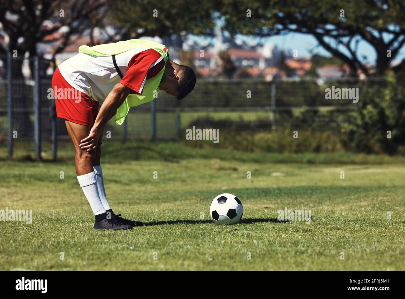 Uomo, stanco e palla di calcio sul campo in allenamento, riscaldamento o allenamento all'aperto in estate. Allenati, calciatore e riposati sul prato in sunshin Foto Stock