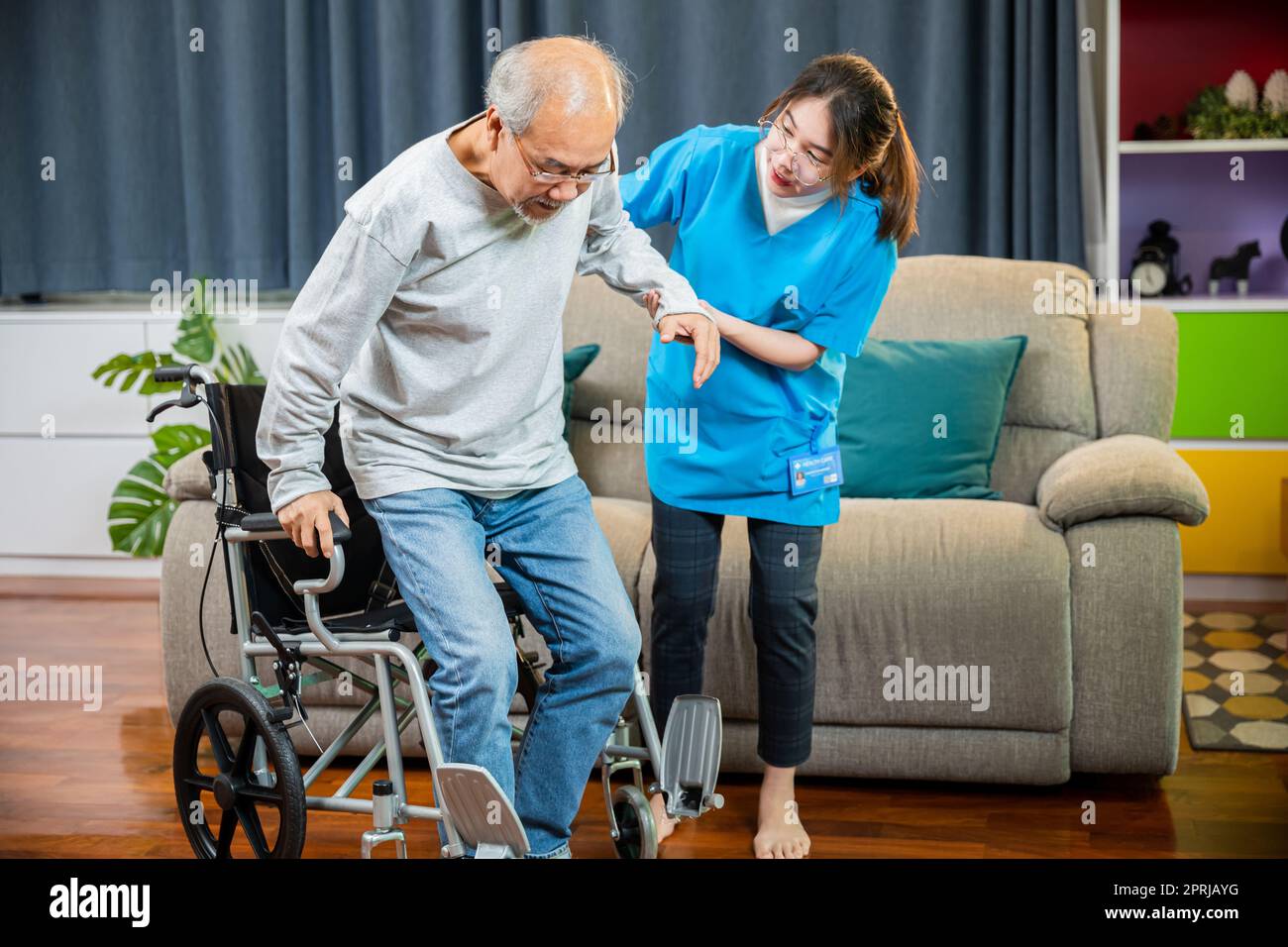 Il medico sostiene l'uomo anziano ad alzarsi per esercitarsi, aiuta gli anziani handicappati in piedi in su Foto Stock