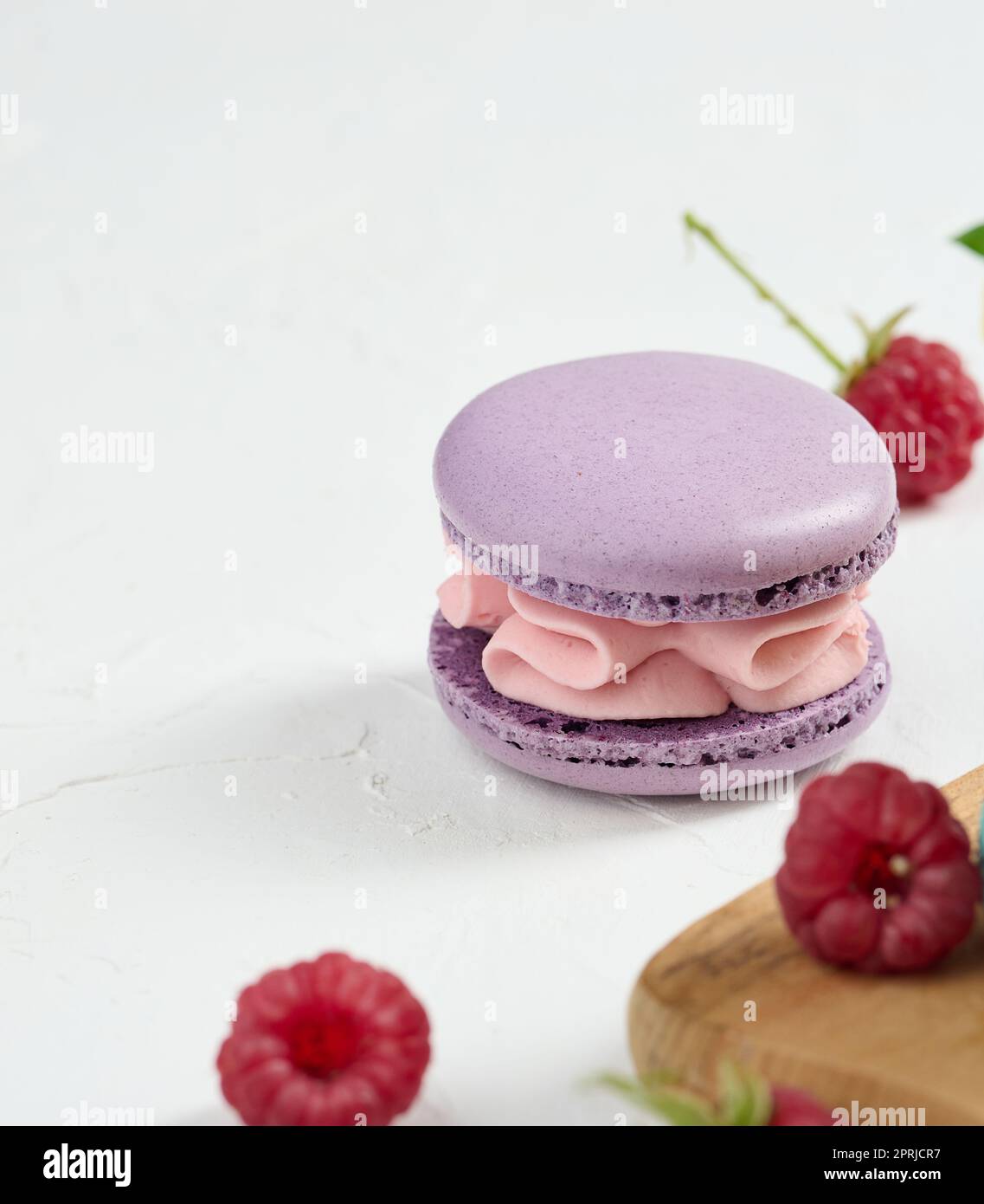 Un macarone viola e lamponi rossi su sfondo bianco Foto Stock