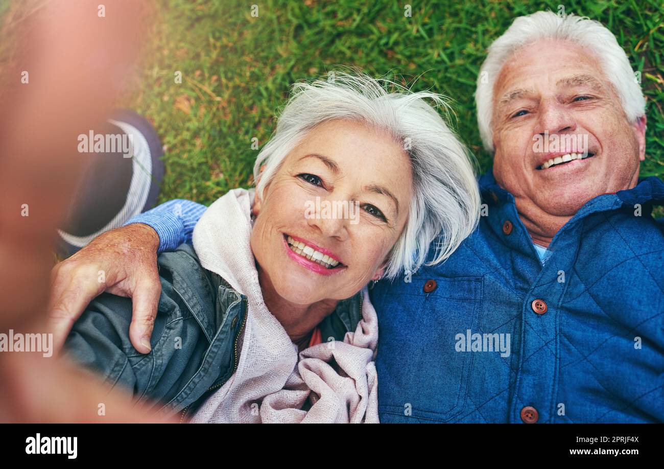 Retirementtime per godere del yourselfie. Una coppia anziana sdraiata sull'erba e prendendo un selfie. Foto Stock