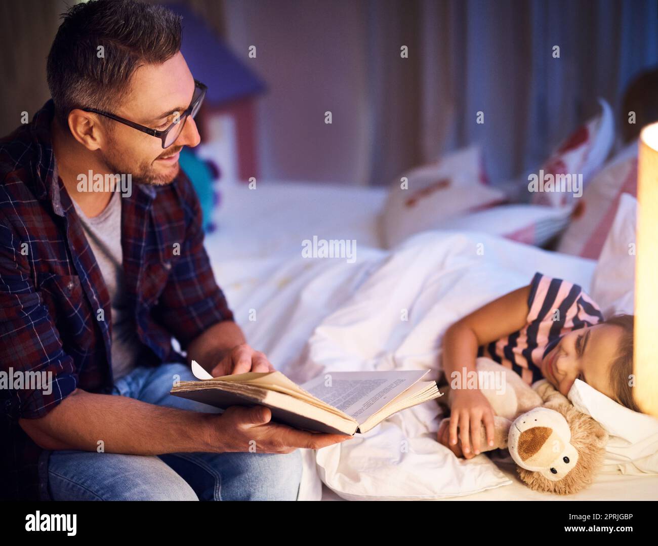 Più. Un padre che legge la sua figlia una storia di bedtime. Foto Stock