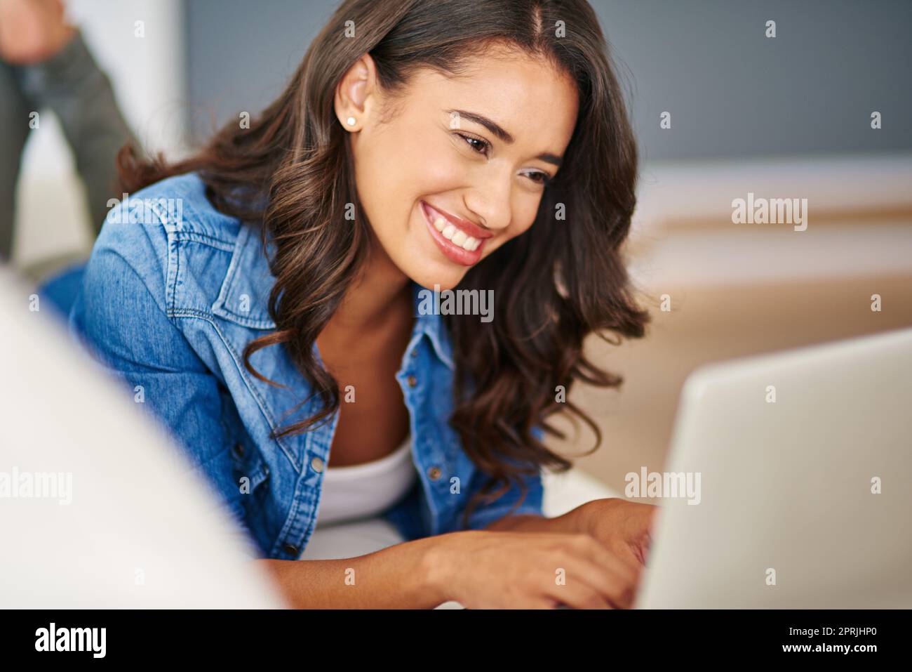 Trovare memi divertenti in rete. Una giovane donna attraente che usa il suo laptop mentre sdraia sul divano. Foto Stock