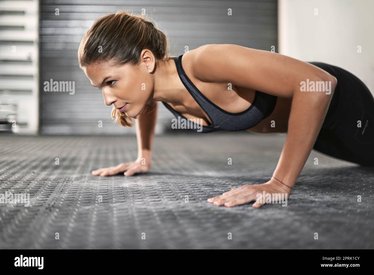 Forte non è solo forza fisica, è una mentalità, una giovane donna che fa i push-up in palestra. Foto Stock