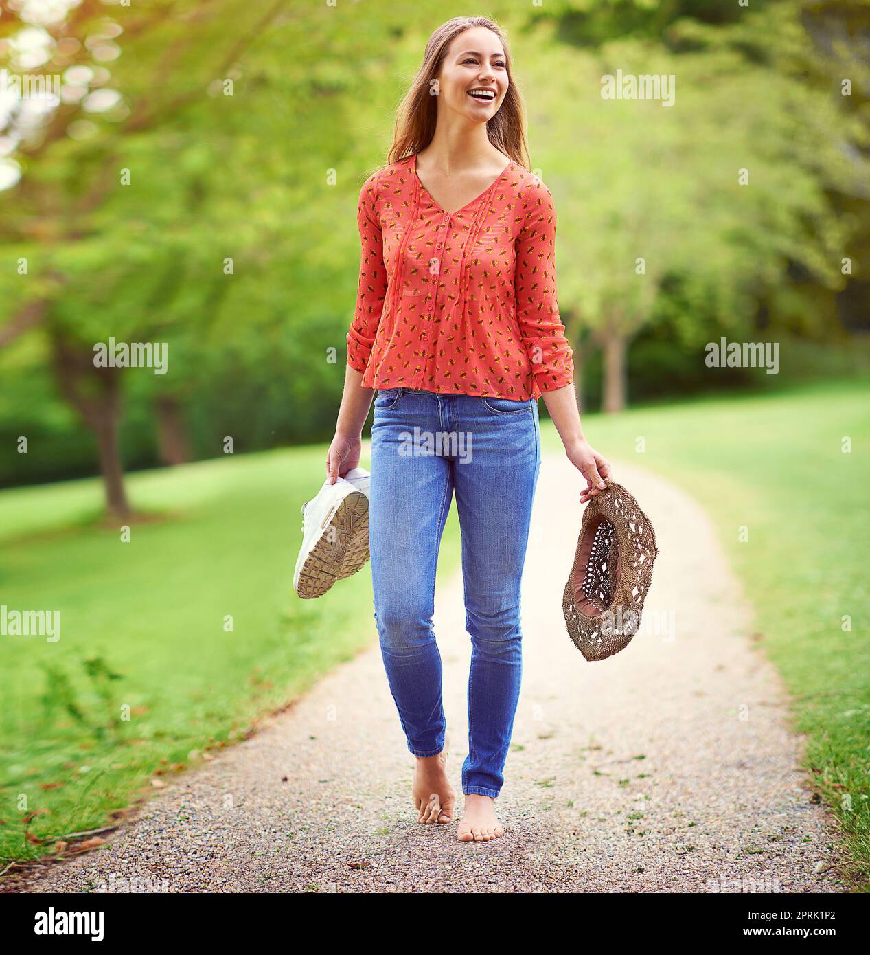 Una di quelle giornate estive spensierate... una giovane donna che cammina in un parco con le scarpe e un cappello. Foto Stock