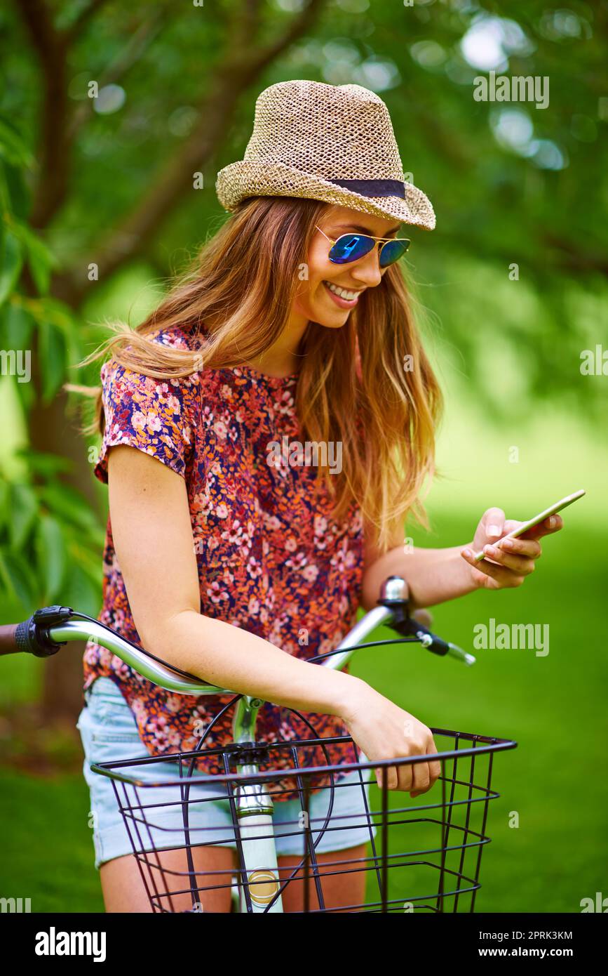 Invitando i suoi amici a unirsi a lei nel parco. Una giovane donna che usa un telefono mentre fuori per una bicicletta nel parco. Foto Stock