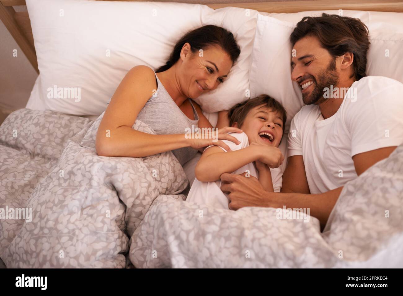 Vuole sempre essere vicino alla mamma e al papà. una giovane famiglia a letto insieme Foto Stock