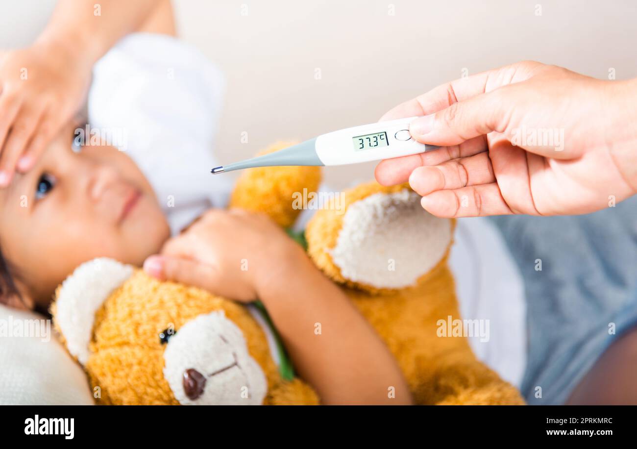 Ragazzo malato. Madre genitore controllo della temperatura della sua figlia ammalata con termometro digitale in bocca, bambino che si stendeva a letto prendendo la misura della sua tempera Foto Stock