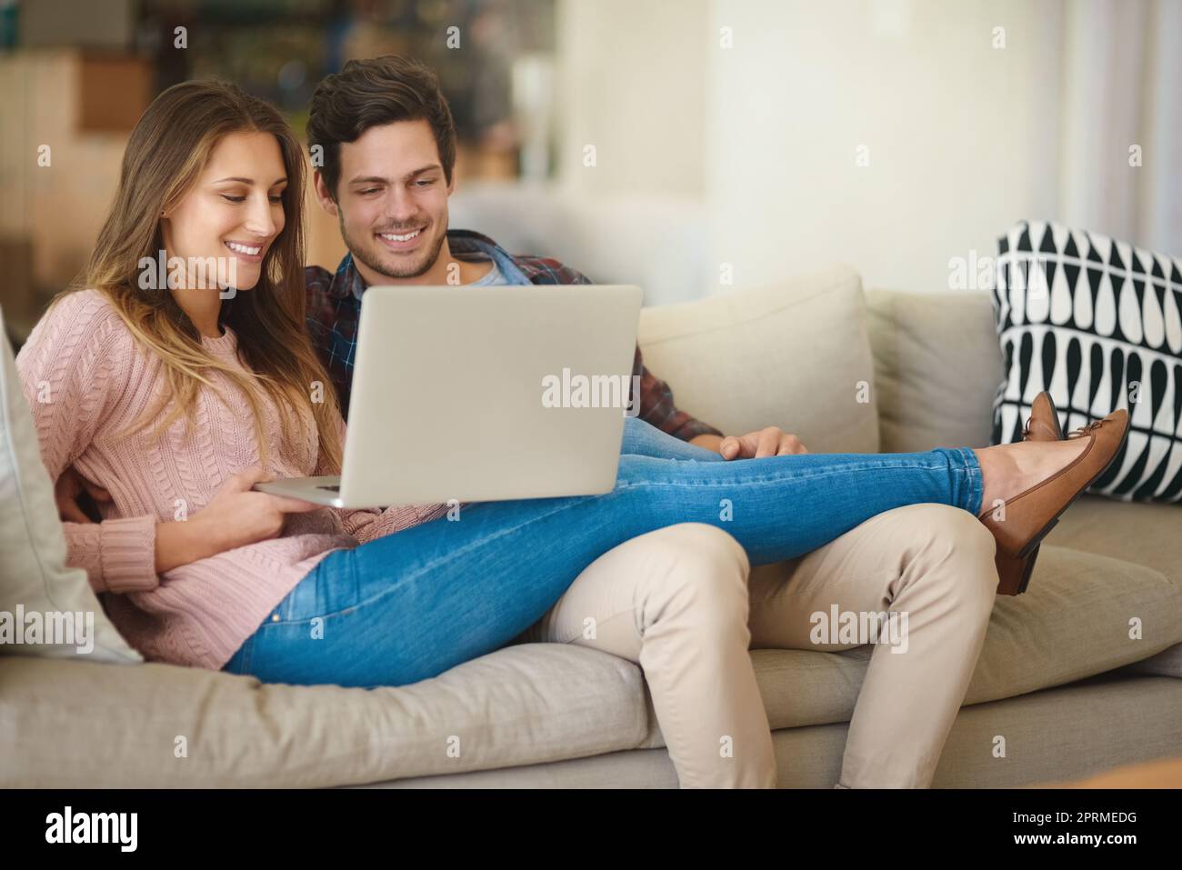Un lavoro leggero con il budget mensile. Una giovane coppia felice che usa un computer portatile insieme mentre si rilassa sul divano di casa. Foto Stock