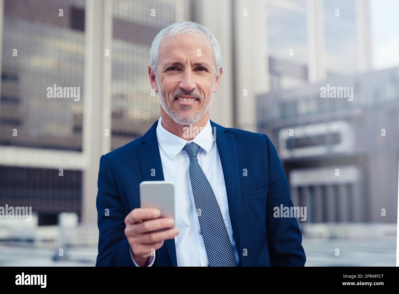 Fidatevi di me, im l'uomo per il lavoro. Ritratto di un uomo d'affari fiducioso che usa il suo cellulare mentre si trova fuori dal suo edificio ufficio. Foto Stock