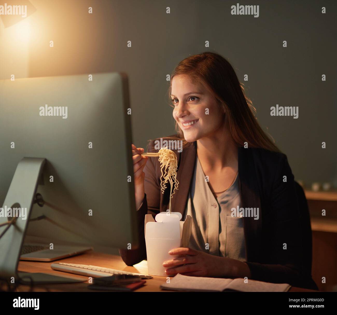 Rifornire la sua mente per una notte tarda. Un giovane designer mangiare da asporto mentre lavora tardi in ufficio. Foto Stock