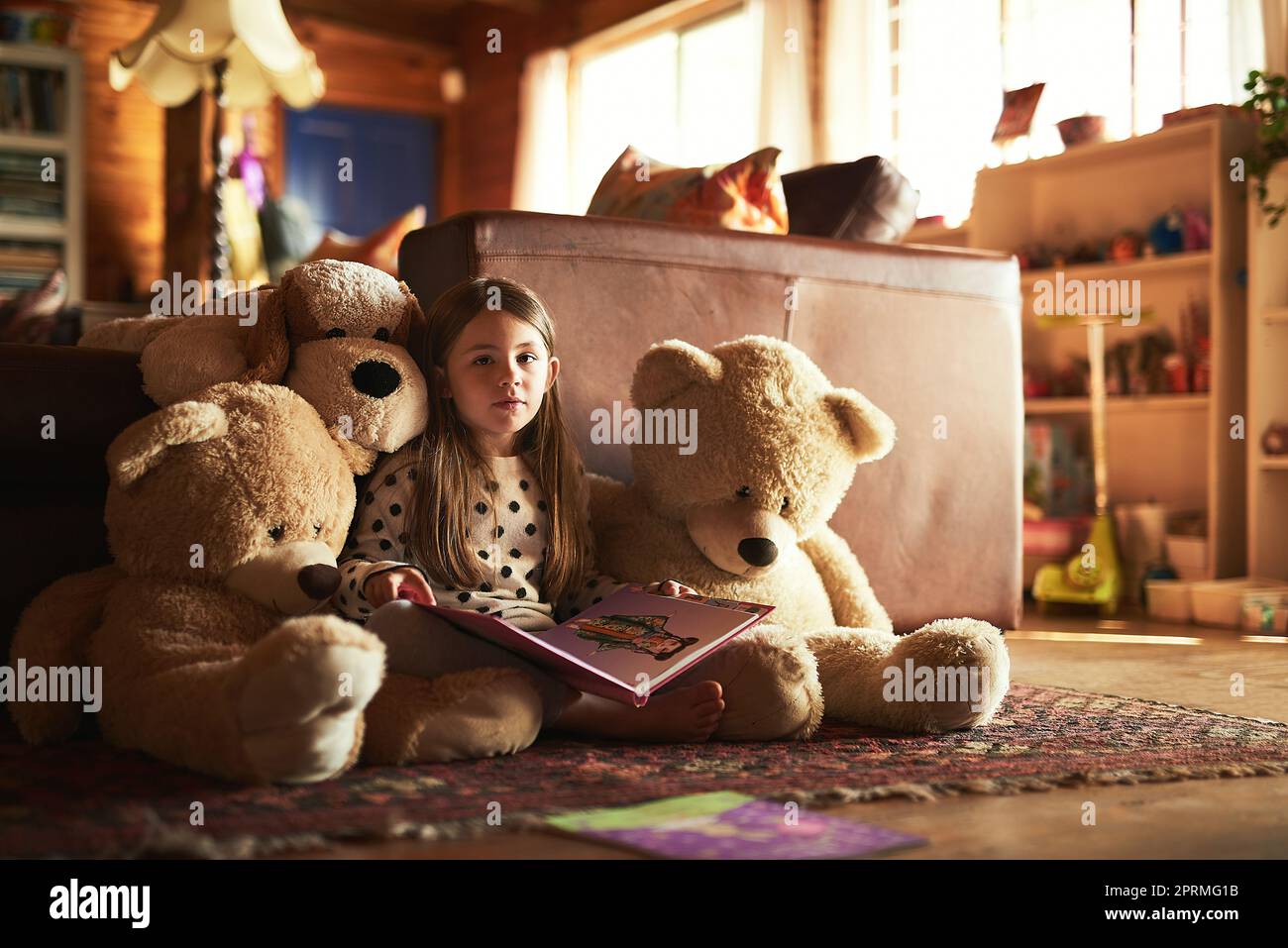 I miei orsacchiotti amano la storia tanto quanto me. Una bambina che legge un libro con i suoi orsacchiotti intorno a lei. Foto Stock