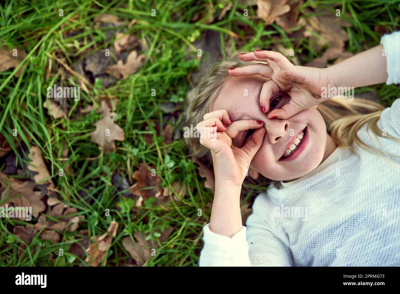 Il mondo è pieno di meraviglia attraverso gli occhi dei bambini. Ritratto di una giovane ragazza sdraiata sull'erba fuori. Foto Stock