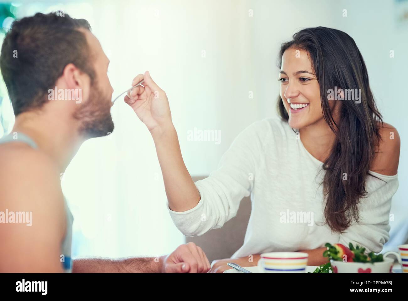 Amerete questo. Una giovane donna felice che allatta il suo ragazzo un boccone della sua colazione a casa. Foto Stock
