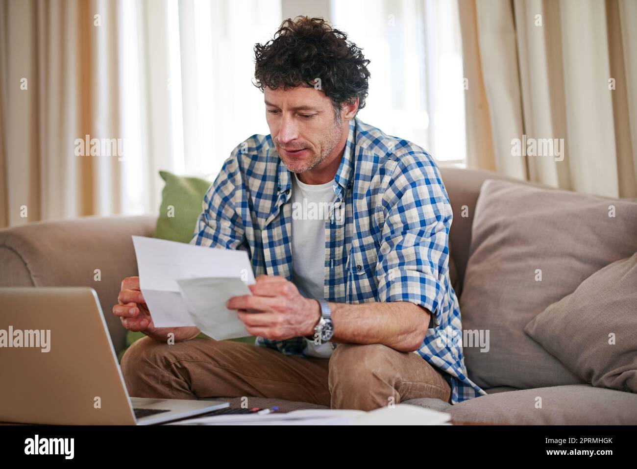 Un uomo maturo che supera le sue spese mentre si siede sul divano a casa. Foto Stock