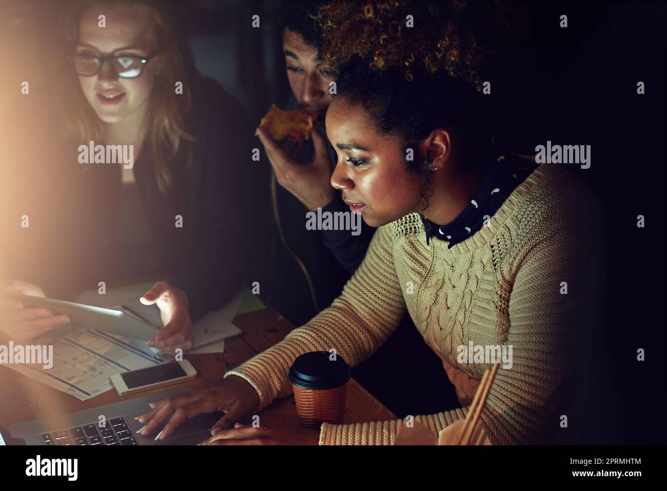 Lavorare contro una scadenza. Un team aziendale che utilizza un notebook insieme durante un turno di notte al lavoro. Foto Stock