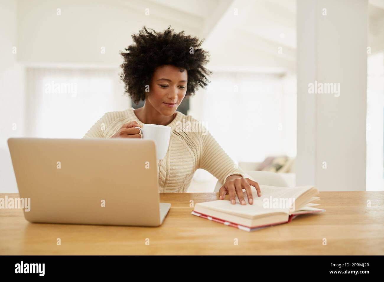 Non ha appena letto. Studia. Un giovane attraente che usa il suo laptop, legge un libro e beve un caffè a casa. Foto Stock