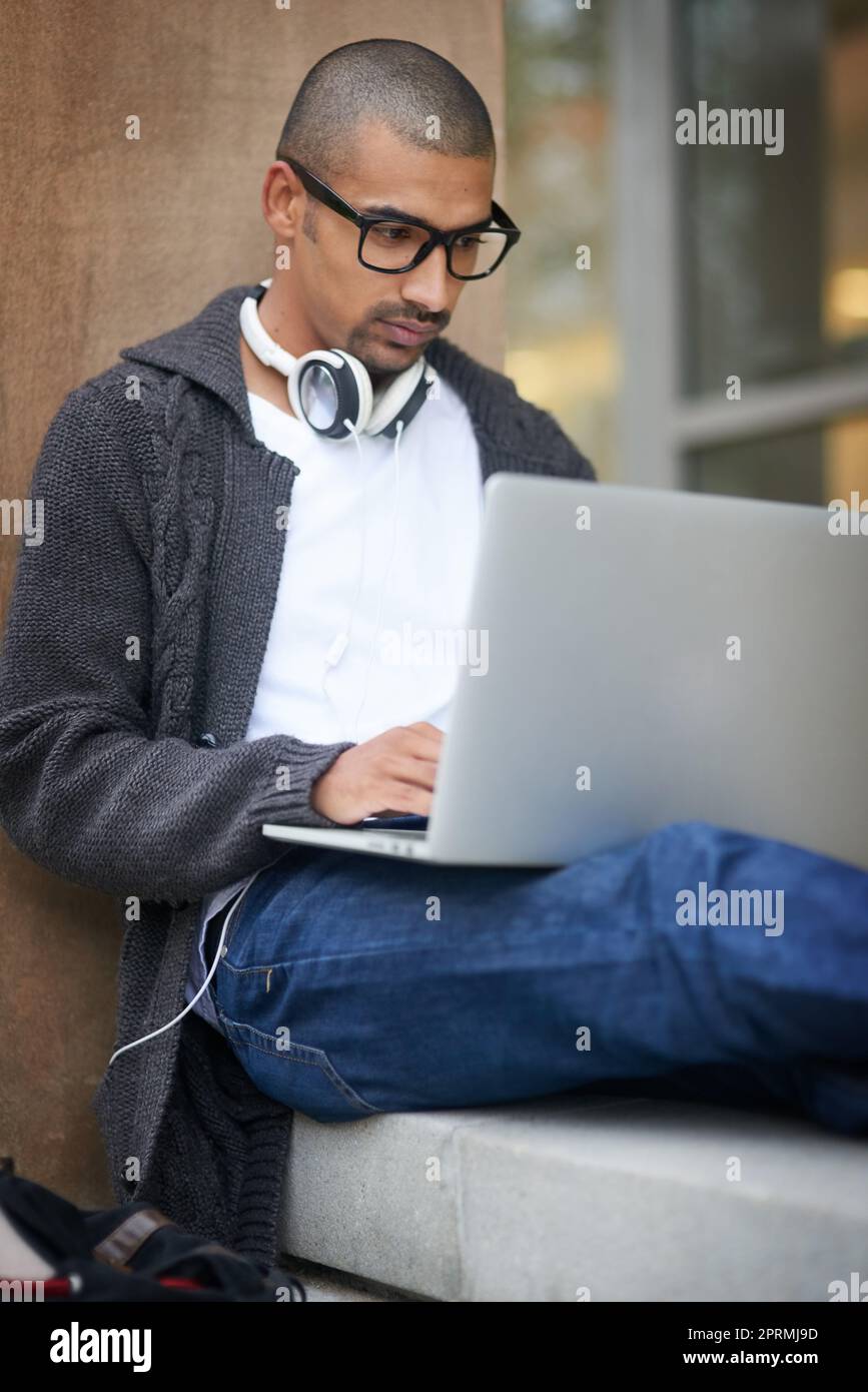 Mostrare dedizione alla sua istruzione. Uno studente universitario che utilizza il suo computer portatile mentre si siede all'esterno del campus. Foto Stock