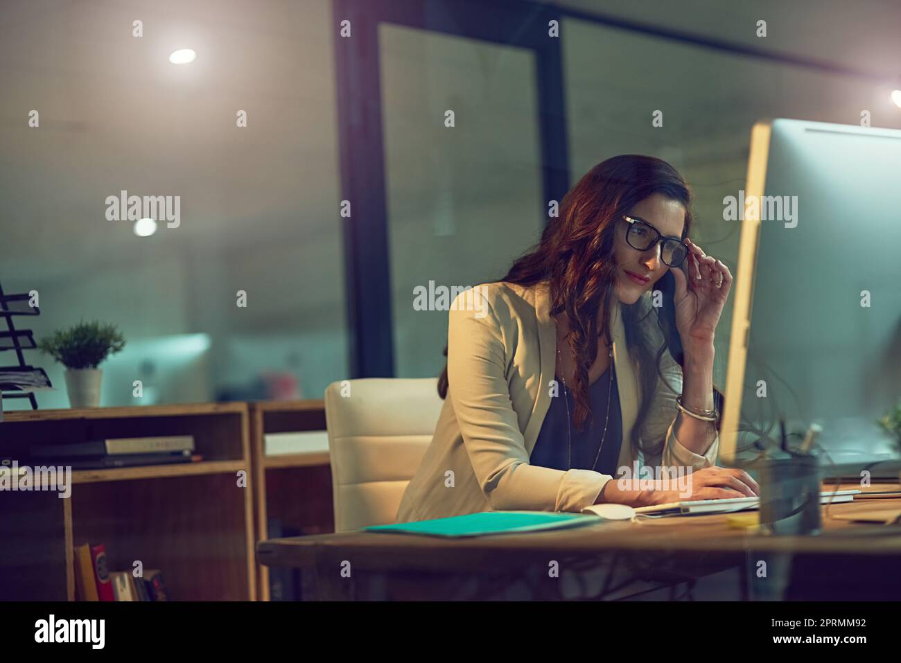 Soddisfare i suoi impegni non importa l'ora. Una giovane donna d'affari che lavora tardi su un computer in un ufficio. Foto Stock