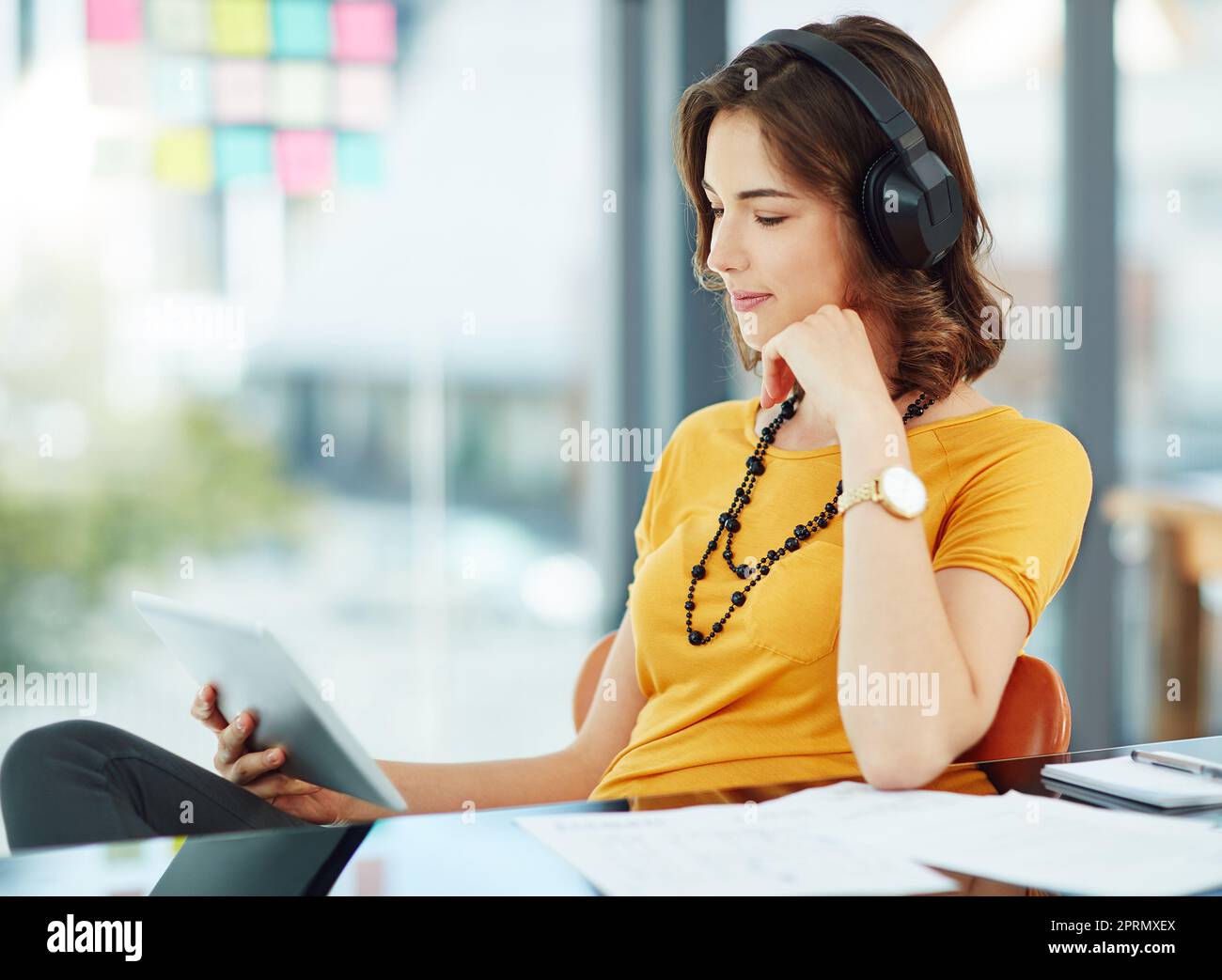 Guardare uno spettacolo nel tempo libero. Una giovane donna d'affari che guarda qualcosa sul suo tablet mentre si siede in ufficio. Foto Stock