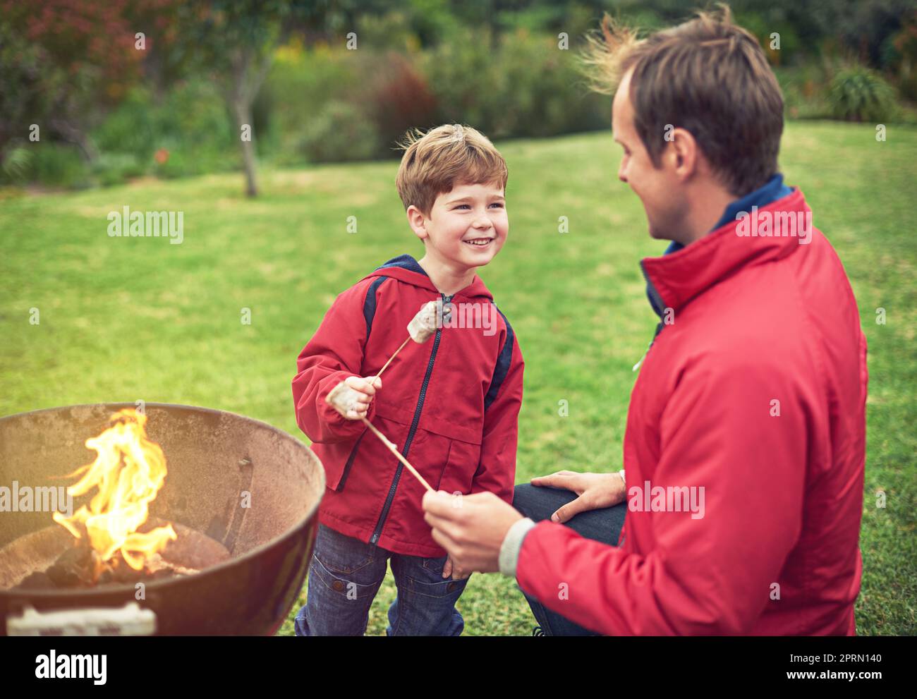 Posso avere anche il tuo, papà. Un padre e un figlio arrostire marshmallows su un fuoco. Foto Stock