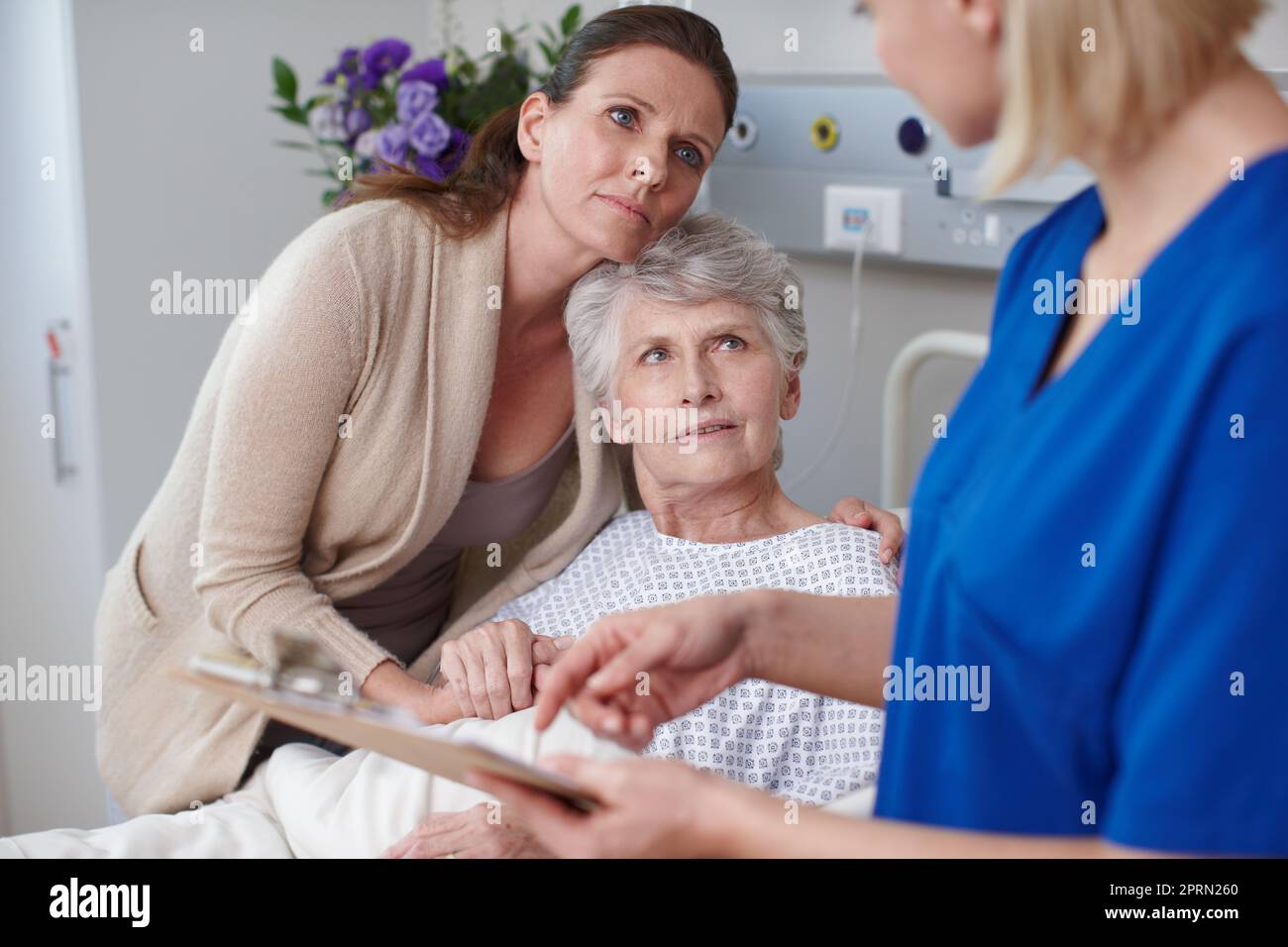 Come potrebbe accadere questo. Una figlia e sua madre che guardano la relazione medica che viene loro mostrata da una giovane infermiera. Foto Stock