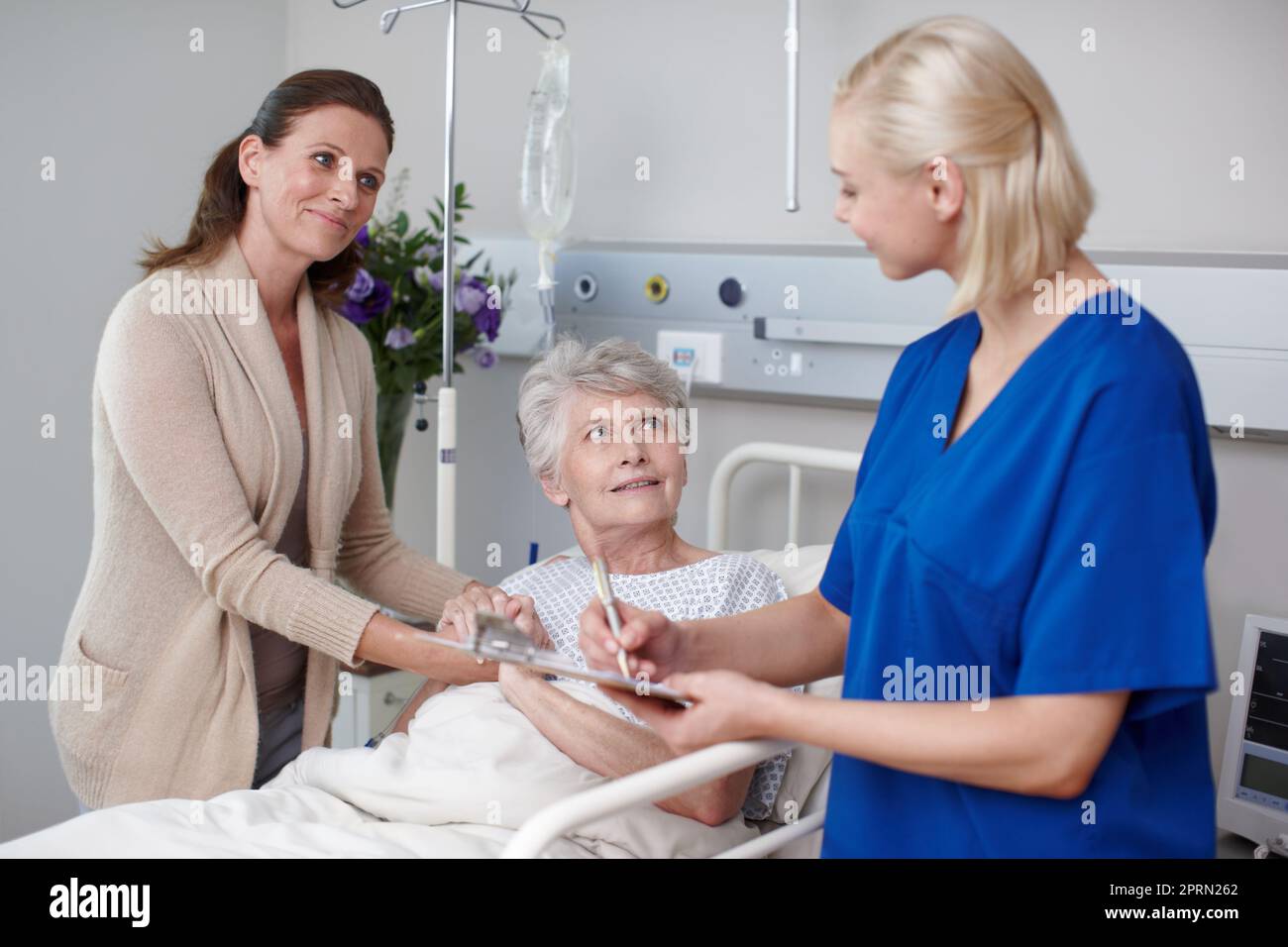 Thats le notizie meravigliose. Una figlia felice e sua madre compilano un modulo medico con l'aiuto di una giovane infermiera. Foto Stock