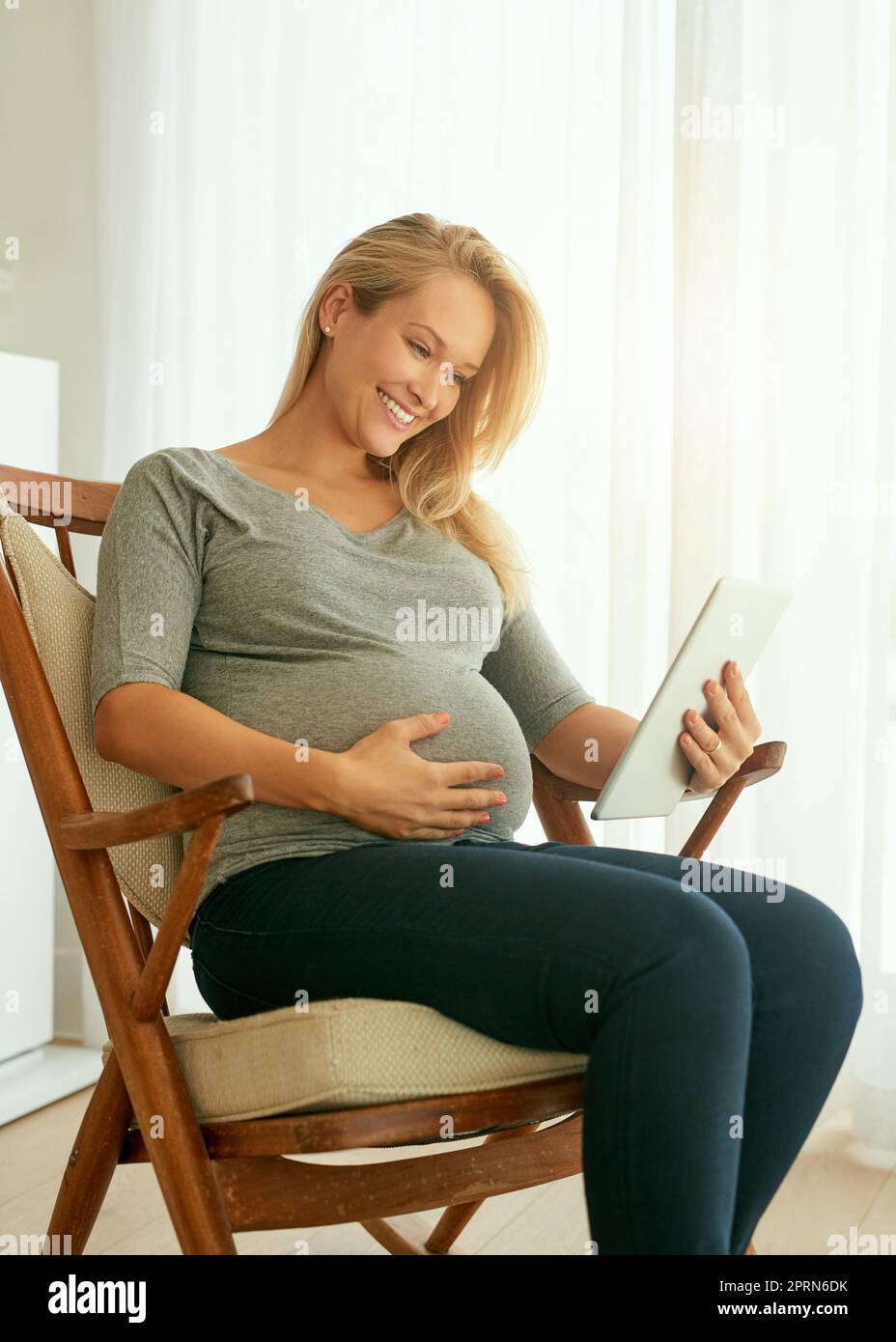 Creare la mia presentazione di gravidanza. una donna incinta che usa il suo tablet digitale seduto su una sedia a dondolo Foto Stock