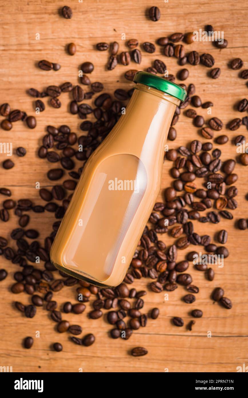 Caffè latte in bottiglia di vetro e caffè in grani sul tavolo di legno. Foto Stock